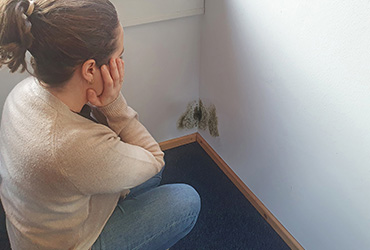 VEINAL_Minimalinvasiv-entfeuchten-1 Eine Frau blickt schockiert auf eine mit Schimmel befallene Wand